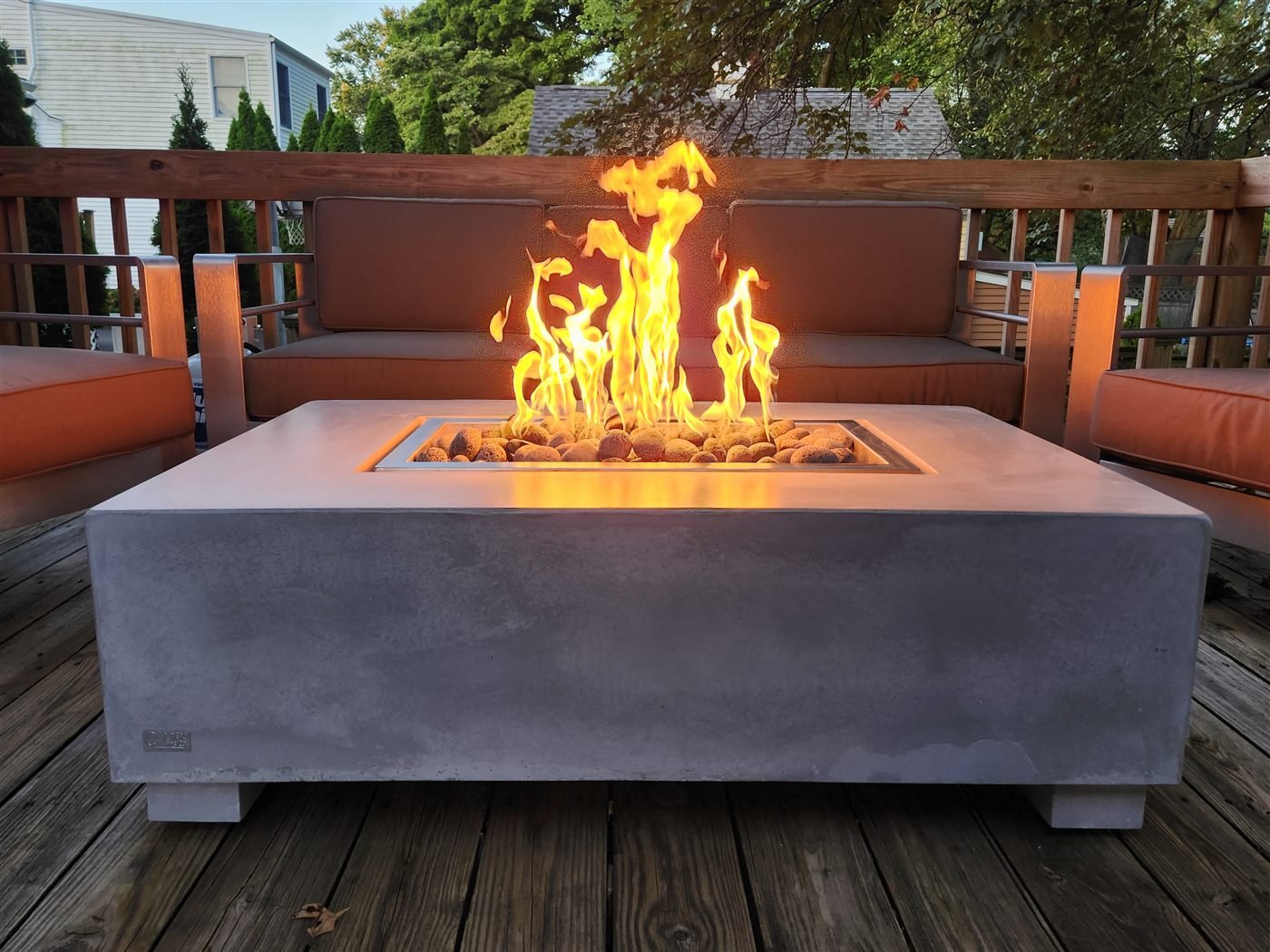 Concrete fire table with tall flame on a deck at dusk